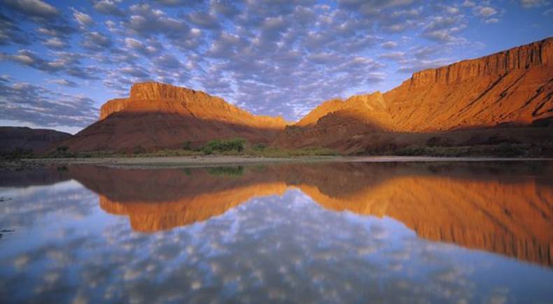 Buttermilk clouds and red cliffs reflected in a river.